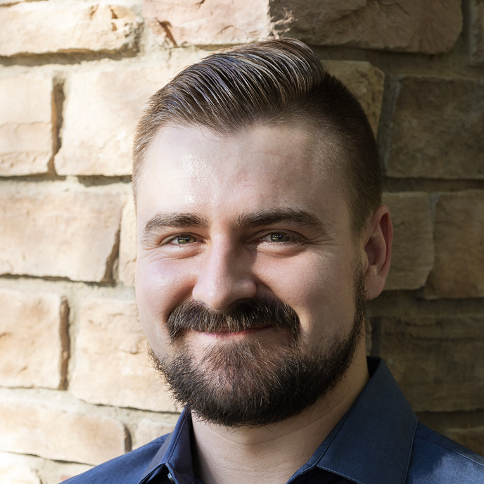 Male smiling in front of light brick wall. 