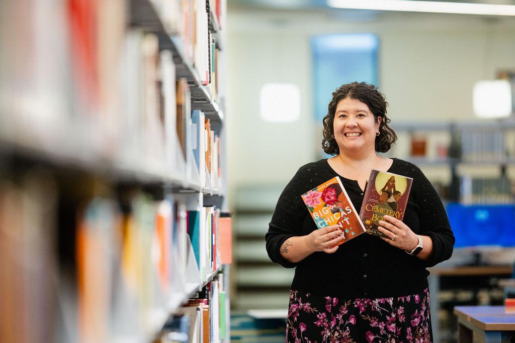 Amanda Takacs, GateWay Faculty Librarian, smiles and shows 2 books she recommends for Hispanic Heritage Month: Big Chicas Don't Cry and Cemetery Boy
