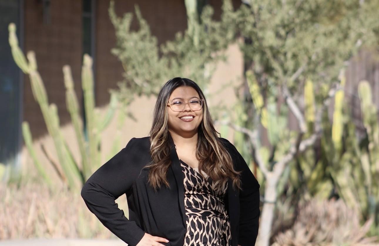 Samantha Kapanak smiles for a photo in front of green trees and cacti.