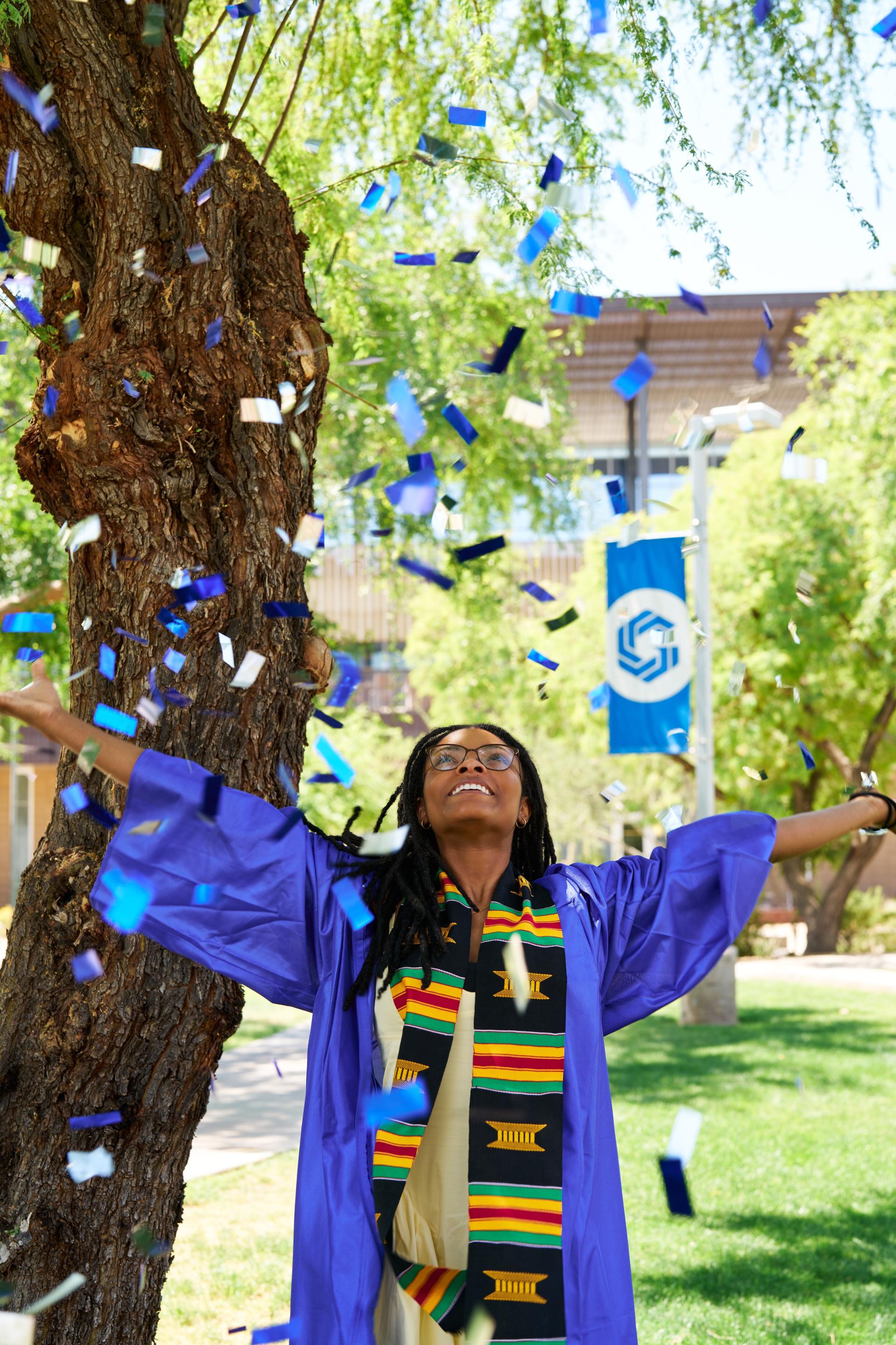 Temya poses on campus in her gown while throwing confetti