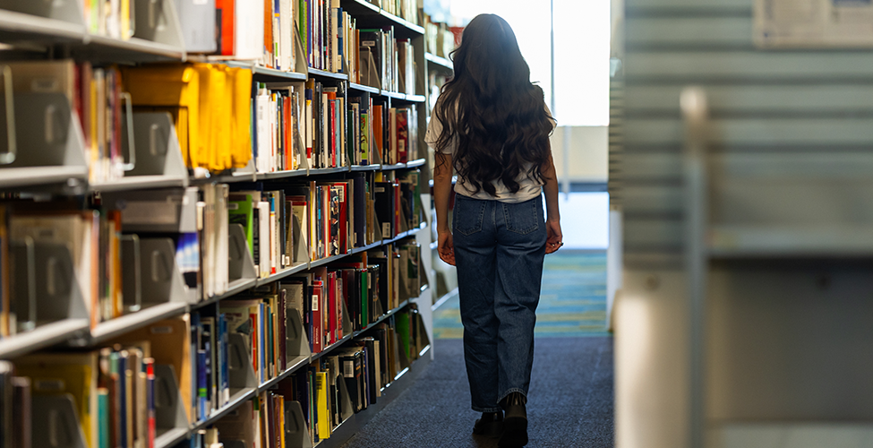Student walking through row of library books