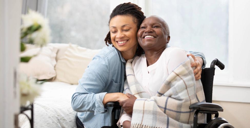 Smiling caregiver hugging a senior woman seated in a wheelchair
