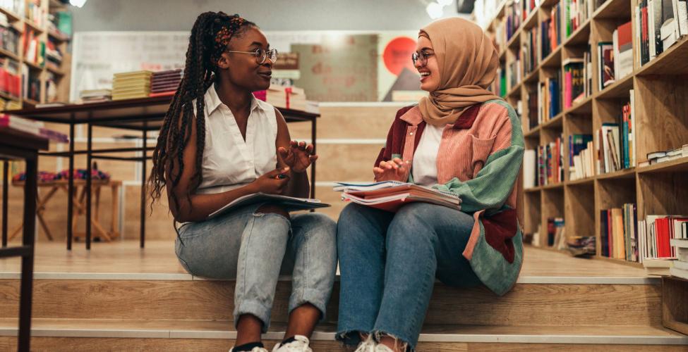 Two college students collaborating and reviewing study notes together inside a campus library