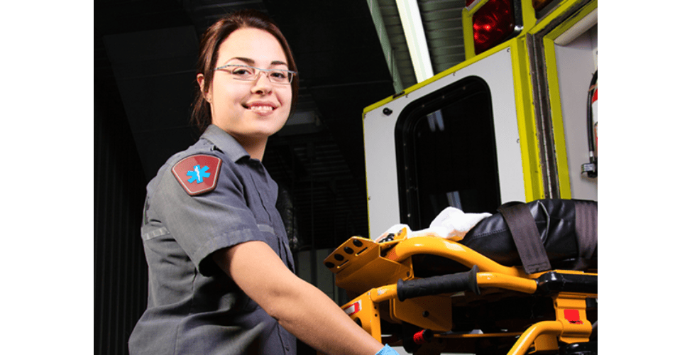 Female EMT technician preparing a stretcher next to an open ambulance.