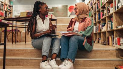 Two college students collaborating and reviewing study notes together inside a campus library