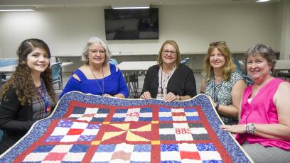 Woman sitting at table showing off their quilt