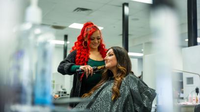 A hairstylist with red hair curls a woman's hair in the GateWay student salon.