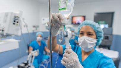 An operating room nurse in blue scrubs checks an IV