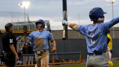 GateWay baseball player number 2 cheers holding a bat while number 3 crosses home plate with the umpire looking on. 
