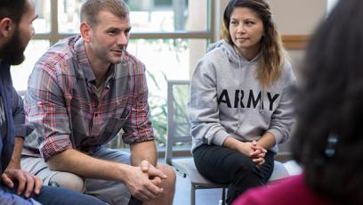 A woman in an Army sweatshirt sits in a workgroup with a white male and two other people. 