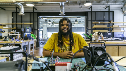 Employee at the Phoenix Forge Makerspace smiles at a table with equipment. 