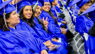 Students in blue caps and gown turn to the camera and smile during the GateWay 2025 Commencement Ceremony