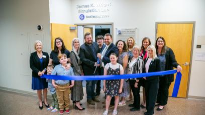 Family and college officials pose together and prepare to cut a blue ribbon in front of the James K. Wright Simulation Lab 