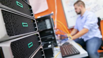 A man works on a computer out of focus with the network computer in focus in the foreground