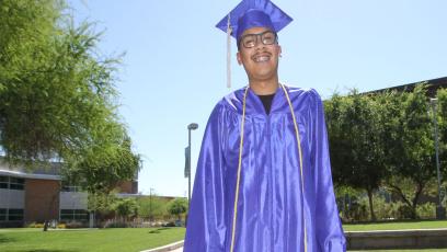 Male student standing on grassy field wearing blue cap and gown
