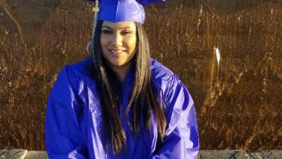Female student sitting on bench wearing blue cap and gown