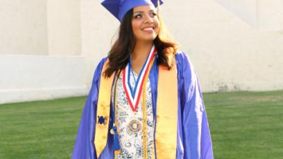 Female student in blue cap and gown with yellow honor stole