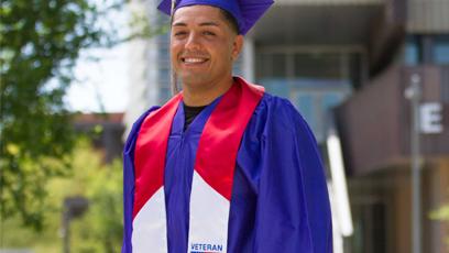 Male graduate wearing blue cap and gown and Veterans stole