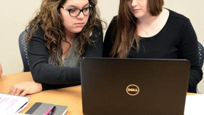 Two female students sitting at desk looking at black laptop computer