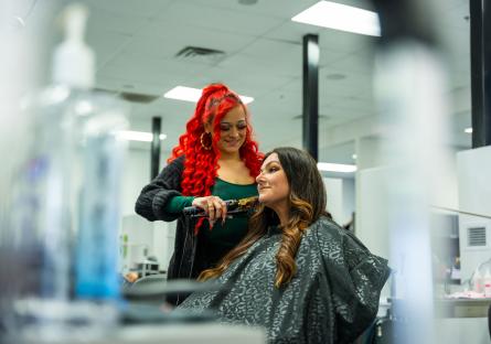A hairstylist with red hair curls a woman's hair in the GateWay student salon.