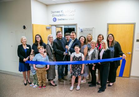 Family and college officials pose together and prepare to cut a blue ribbon in front of the James K. Wright Simulation Lab 
