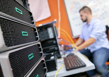 A man works on a computer out of focus with the network computer in focus in the foreground