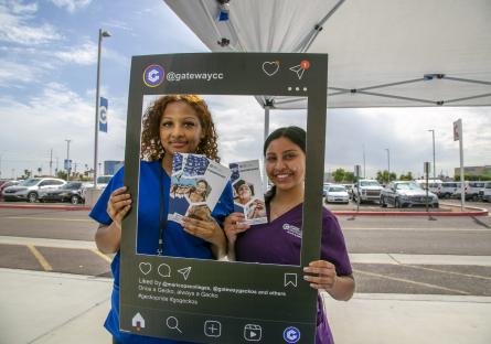 Two female GateWay students wearing scrubs pose with an Instagram frame. 
