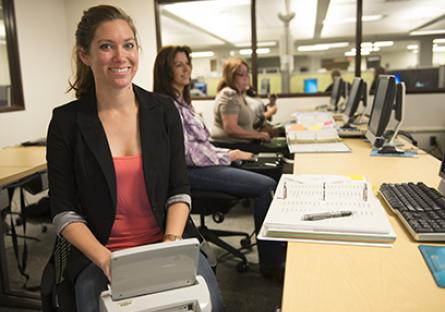 A smiling woman types at her steno machine in class