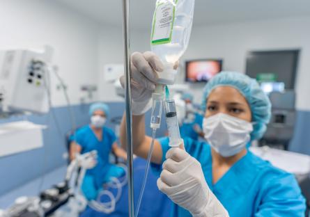 An operating room nurse in blue scrubs checks an IV