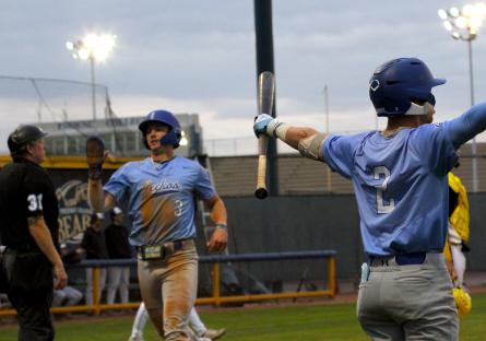 GateWay baseball player number 2 cheers holding a bat while number 3 crosses home plate with the umpire looking on. 