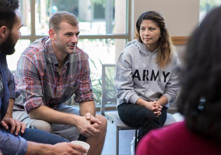 A woman in an Army sweatshirt sits in a workgroup with a white male and two other people. 
