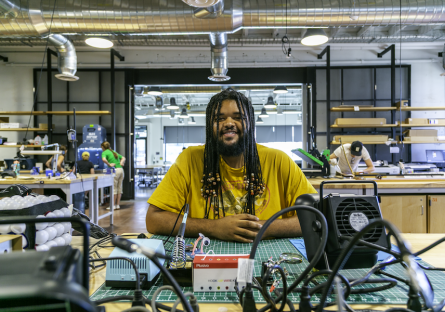 Employee at the Phoenix Forge Makerspace smiles at a table with equipment. 