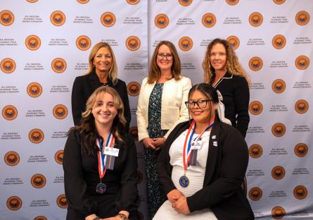 Students Samantha and Elisa take a photo with GateWay Community College President and faculty in front of a backdrop. 