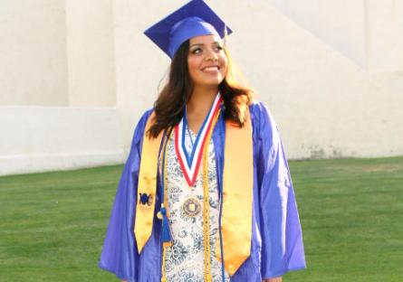 Female student in blue cap and gown with yellow honor stole