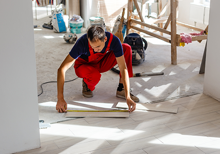Person installing flooring, measuring and aligning planks during a hands-on construction project.