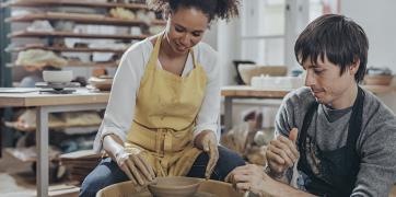 Photograph of woman sitting down near a pottery where with a male sitting next to her. 
