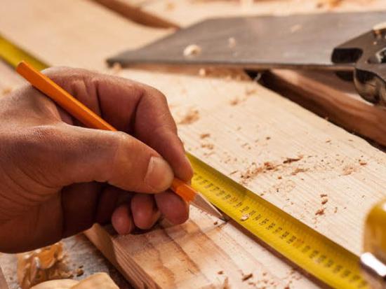 Close-up of a carpenter using a pencil and tape measure to mark a wooden board