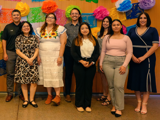 A group of eight smiling college representatives standing in front of colorful festive decorations
