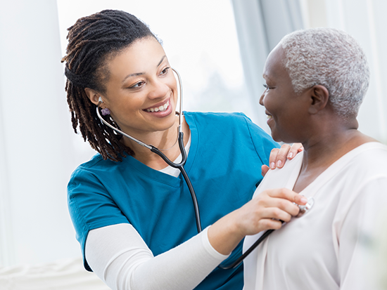 Female nurse wearing scrubs sitting next to female patient. 