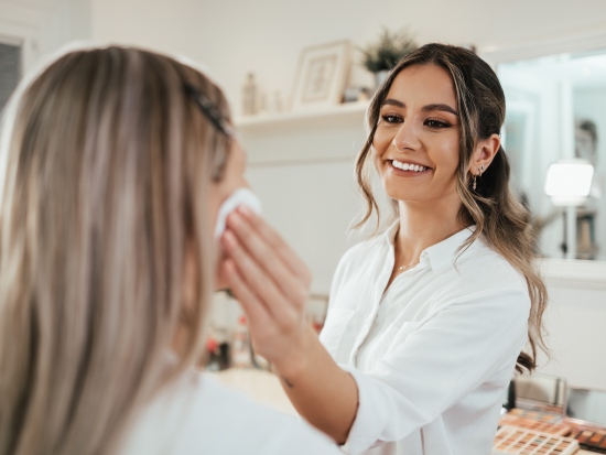 Woman applying lotion to customer face with white cotton round