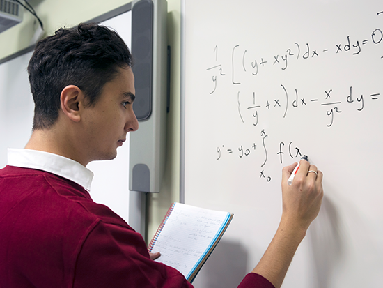 Young man at white board doing math equations