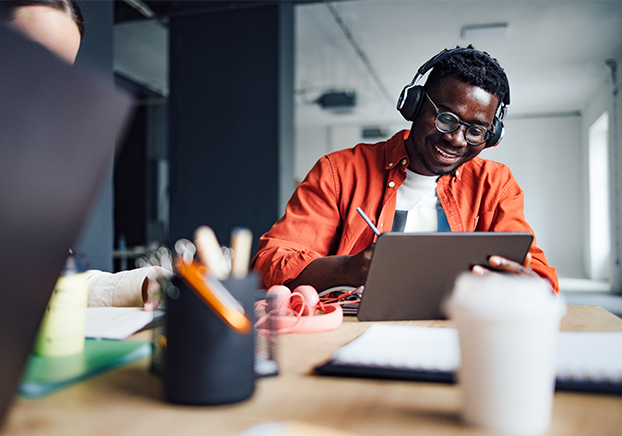 Male student wearing orange shirt and headphones sitting at desk.