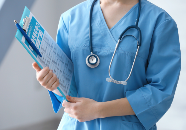 A medical worker wearing scrubs and a stethoscope, holding a medical chart.