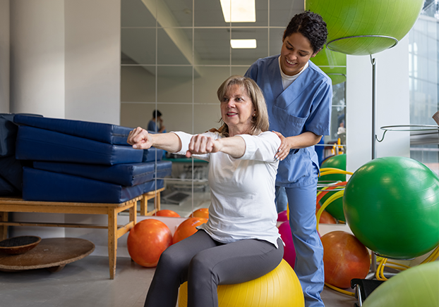 PTA student working with female patient sitting on yellow work out ball.