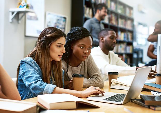 Two women focused working on a laptop and an individual beside them studying