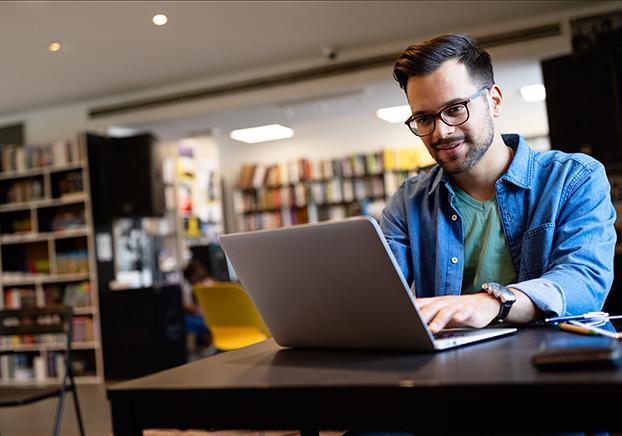 A man typing on a laptop computer in a library.