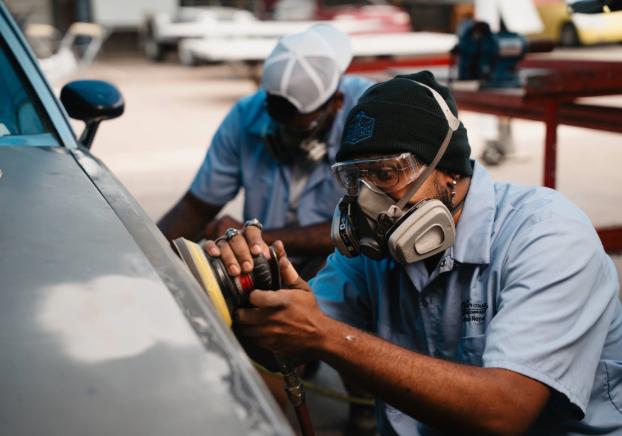 Student sanding a car panel with safety gear in an automotive collision repair class