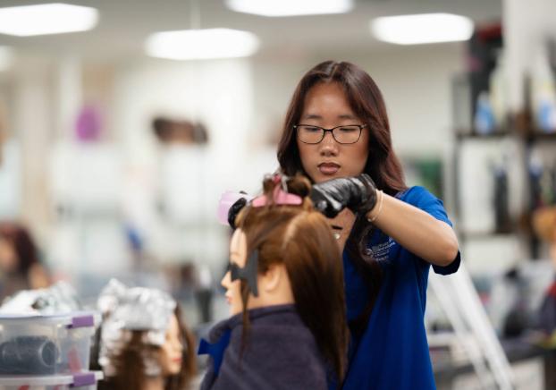 Cosmetology student working on a training mannequin in a salon classroom