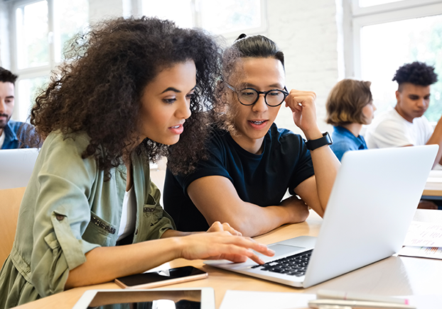 Two students sitting at desk looking at laptop