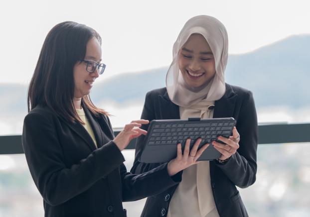 Two professional women collaborating on a digital tablet in an office setting.